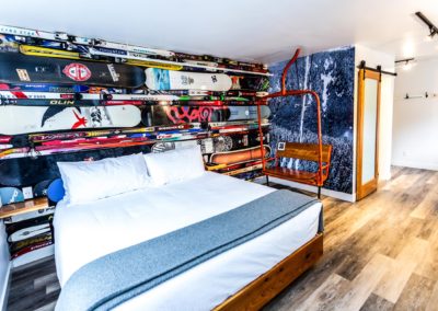 Winter sports inspired back wall with skis and snowboards attached and a single bed in the room with an antique chair lift next to the bed. | The Crash Hotel Squamish