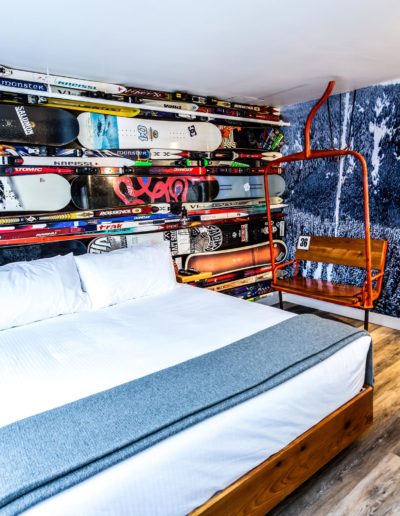 Winter sports inspired back wall with skis and snowboards attached and a single bed in the room with an antique chair lift next to the bed. | The Crash Hotel Squamish