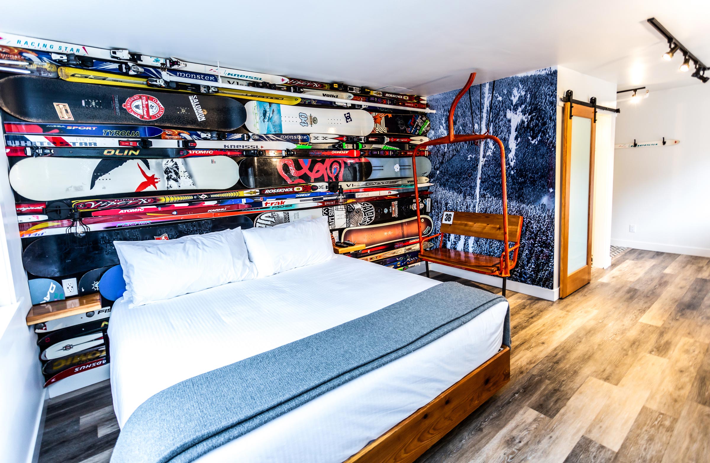 Winter sports inspired back wall with skis and snowboards attached and a single bed in the room with an antique chair lift next to the bed. | The Crash Hotel Squamish